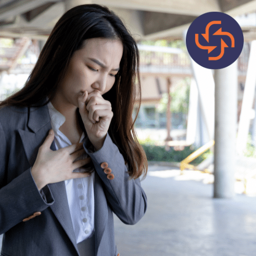 Young woman in a gray blazer clutching her chest and coughing, showing signs of respiratory or heart-related discomfort.
