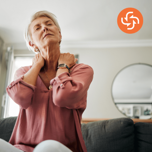 Senior woman sitting on a couch holding her neck in pain, suffering from stiffness or discomfort.