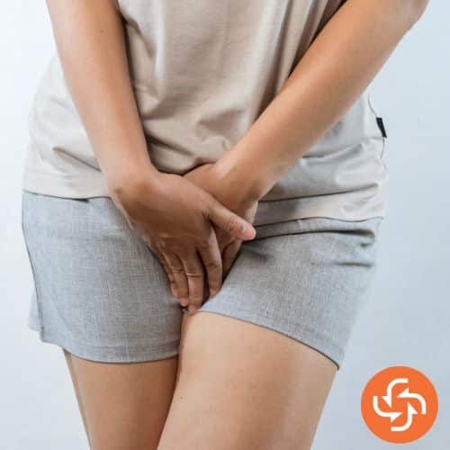 Woman in shorts holding her lower abdomen and pelvic area, indicating discomfort or urinary problem.