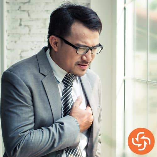 Man in suit clutching chest with a pained expression, showing possible chest pain from pain.