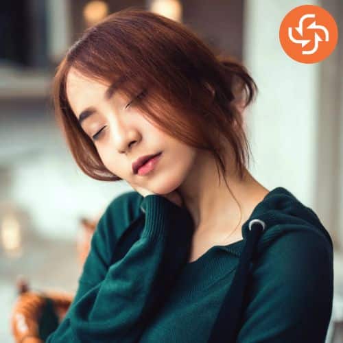 Young woman in a green hoodie with eyes closed and head tilted, showing signs of tiredness or fatigue.