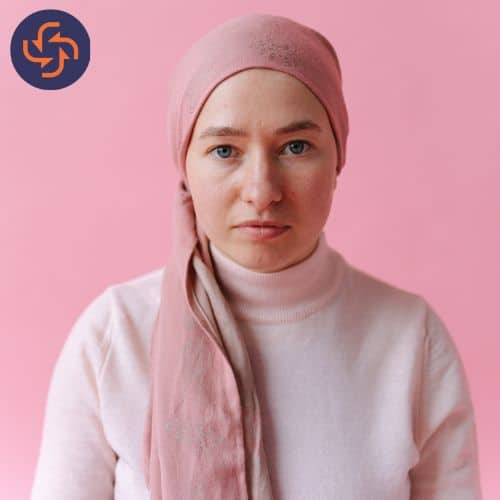Woman wearing a pink headscarf and sweater, symbolizing breast cancer awareness and support.