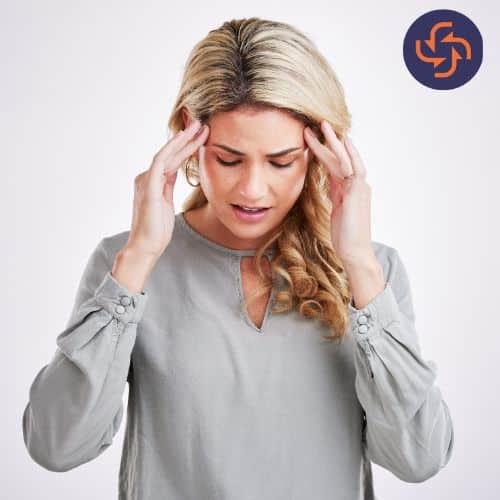 Woman holding her temples with both hands, eyes closed, appearing to suffer from a headache or migraine.