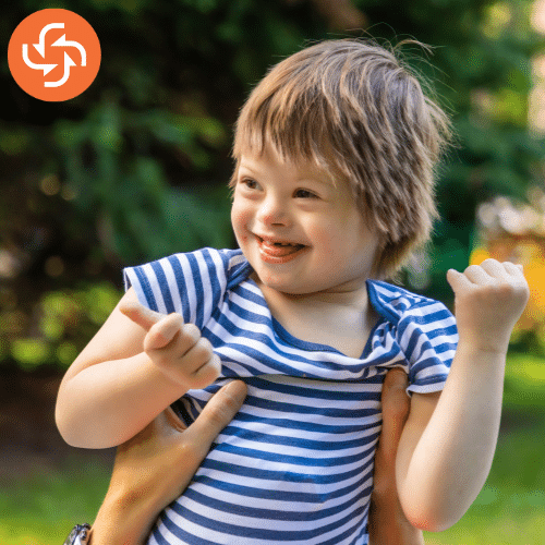 Happy young child in a striped shirt smiling while being held outdoors, representing joy, inclusivity, and care.