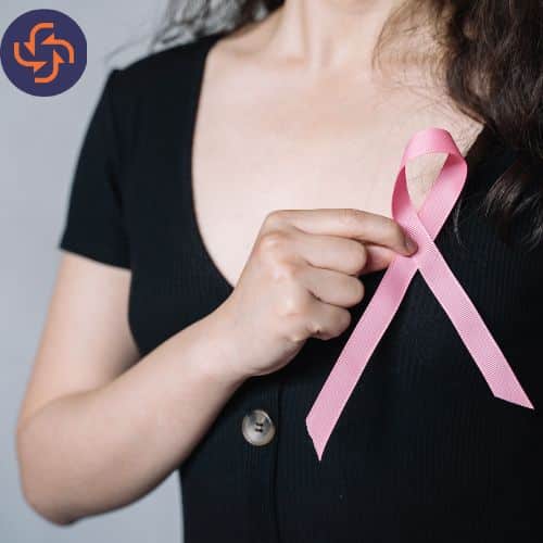 Woman wearing a black top holding a pink ribbon, symbol of breast cancer awareness.