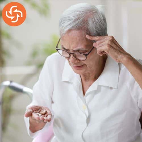 Older adult examining pills while touching temple.