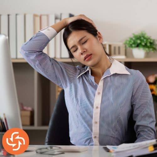 Woman stretching her neck while sitting at a desk.