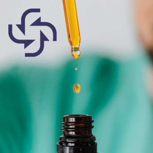 A glass dropper dispensing a single amber-colored liquid drop into a small dark glass bottle, with a dark purple circular arrow logo in the top left corner against a blurred green background.