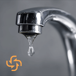 A close-up of a chrome water faucet with a single clear drop of water hanging from the nozzle, featuring a small orange circular arrow logo in the bottom left corner.